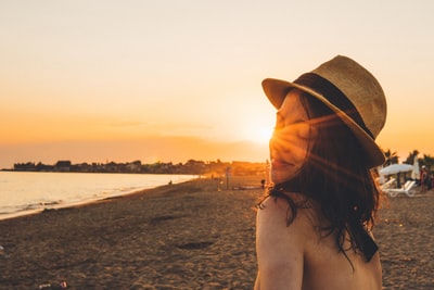 日落时，戴着棕色太阳帽的女人站在海滩上